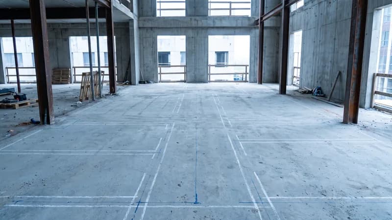 Printed layout lines marking wall positions across the concrete slab of an unfinished building floor.